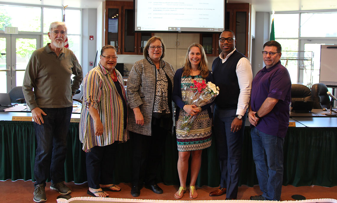 Woman holding flowers surrounded by five other people congratulating her.