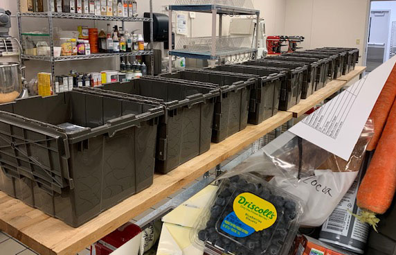 Black plastic containers in a row with assorted food in the bottom right corner