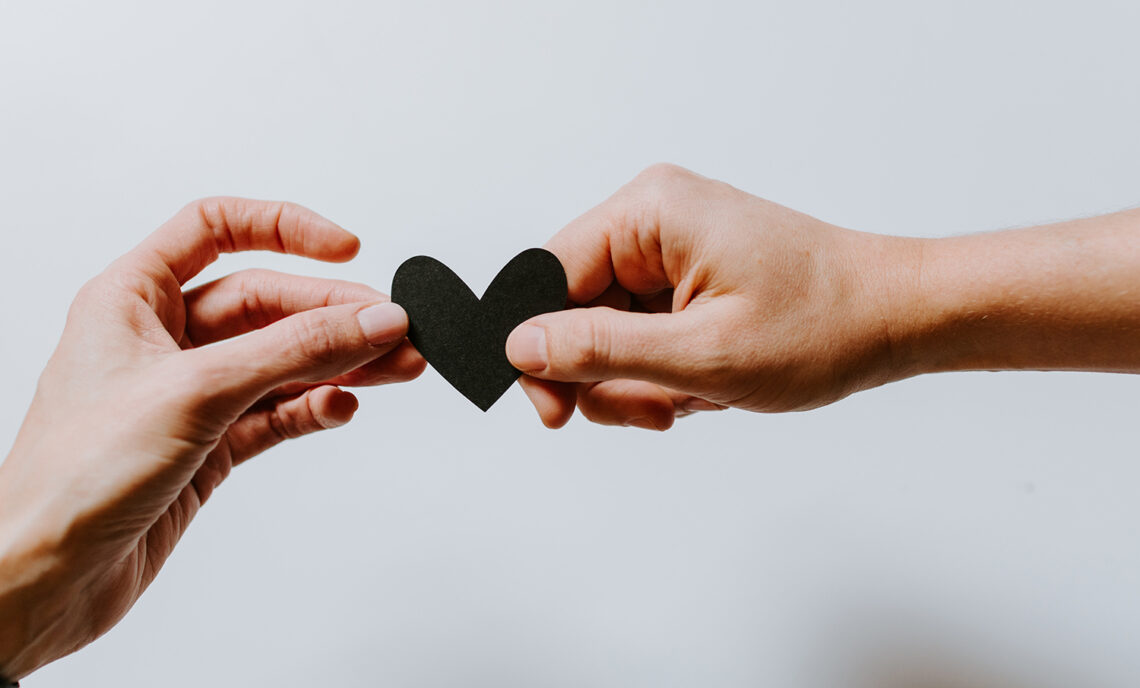 two hands holding a black paper heart cut out