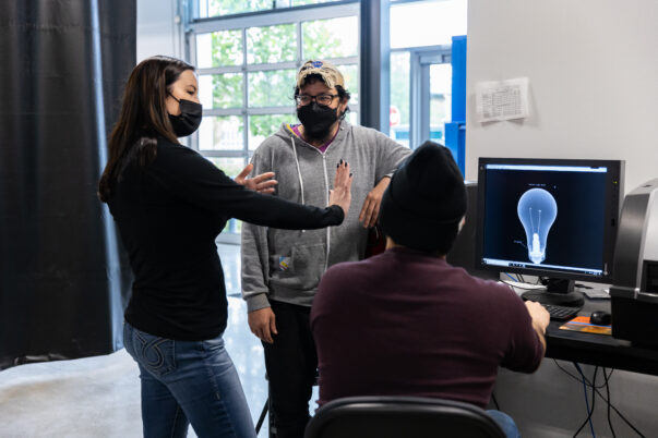 Megan Davey talking with two male students in from of a computer with a lightbulb on the screen