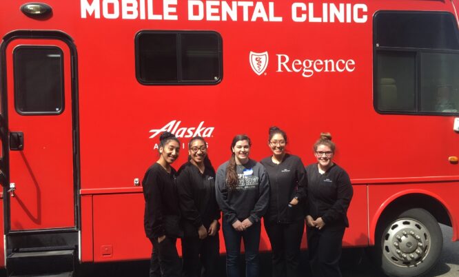 Mobile dental clinic van with dental assistant program students standing next to it.