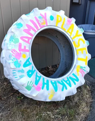 Large painted tire with the text Nakahara Family Playset and child handprints