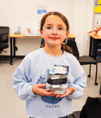 a young girl wearing glasses shows off her classroom project