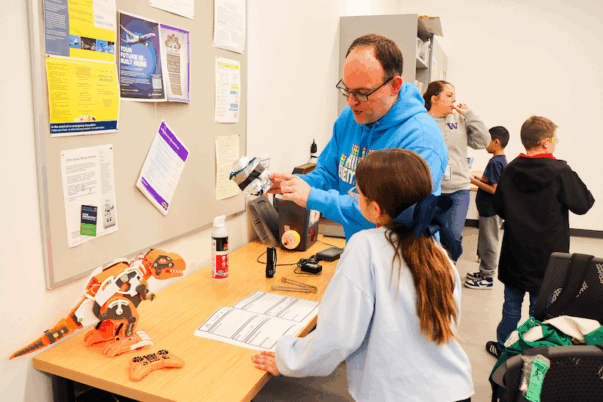 a teacher shows a student a robot in a classroom while others stand in the background