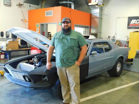 Nick Eilers proudly poses next to his own car, one of the projects for the students